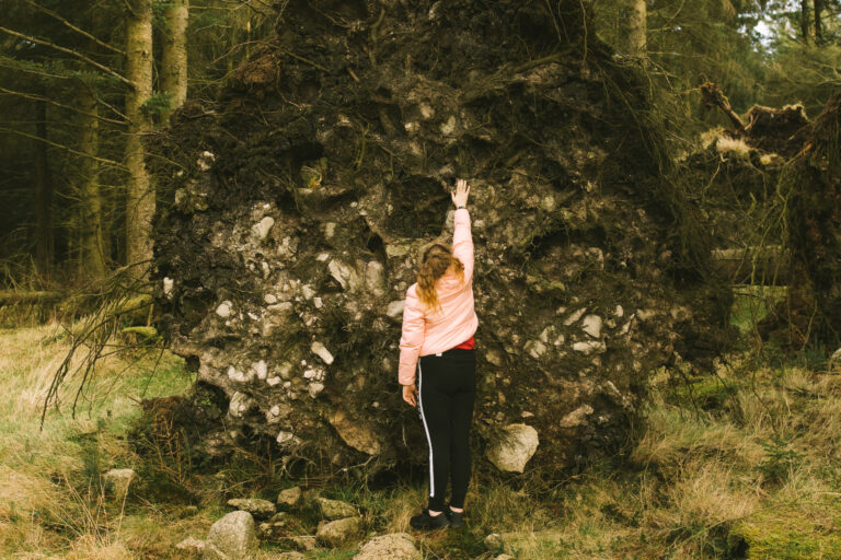 A young child reaches her arm up to see how tall a fallen tree root